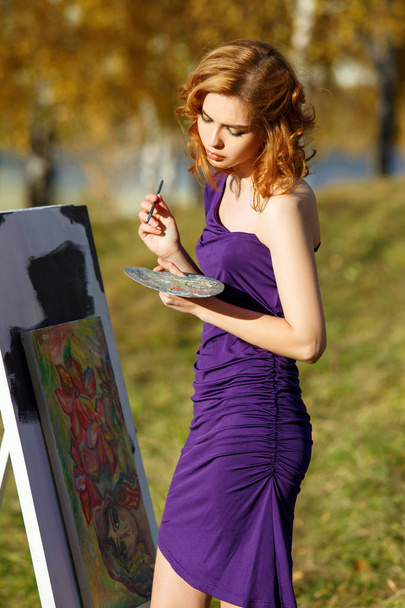 schöne Frau in lila Kleid Malerei im Freien im herbstlichen Park. - Foto, Bild
