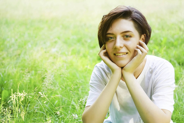 Beautiful portrait of pensive young short haired girl on blurred green grass meadow background, closeup. empty copy space for inscription. happy smiley face. - Zdjęcie, obraz