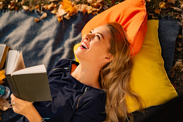 jeune femelle dans le parc d'automne. Une femme dans un parc d'automne lit un livre, allongée sur un plaid, plaisir de lire à l'automne
. - Photo, image