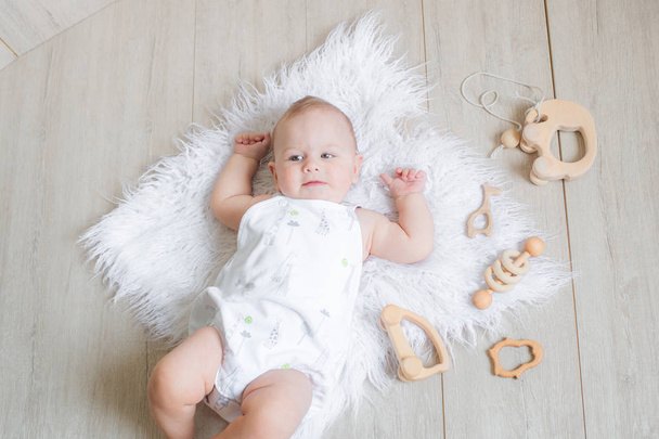 A lovely cute newborn baby lies on a white rug and plays the first eco-tree toys. The concept of family and healthy motherhood - Fotó, kép