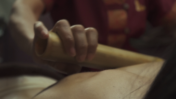 Молодая женщина, лежащая на деревянной кровати спа, имеет бамбуковые палочки для массажа тела. Крупный план
. - Кадры, видео
