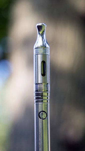 Elektronikus cigaretta kannabiszolajjal homályos természetes háttérrel - Fotó, kép