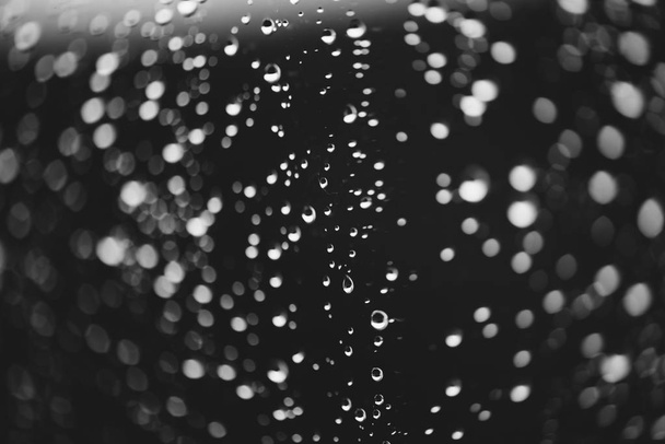 Dirty window glass with drops of rain. Atmospheric monochrome dark background with raindrops in bokeh. Droplets and stains close up. Detailed transparent texture in macro. Copy space. Rainy weather. - 写真・画像