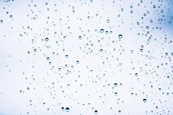Dirty window glass with drops of rain. Atmospheric blue light background with raindrops. Droplets and stains close up. Detailed transparent texture in macro with copy space. Rainy weather. - Photo, Image
