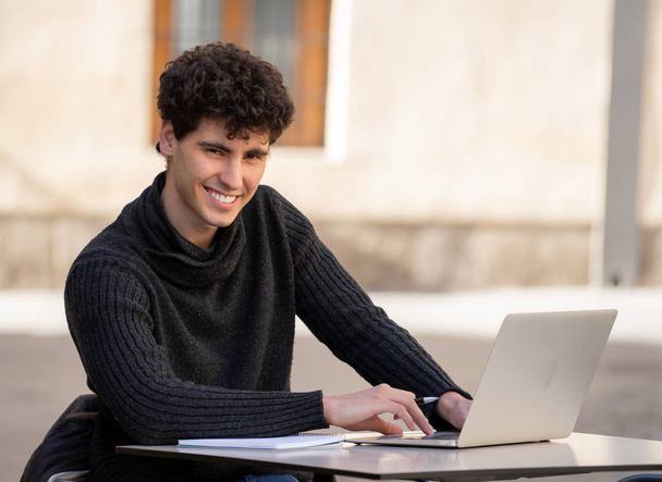 Handsome young man working on laptop computer outside terrace in an european city coffee shop. Student Feeling happy and satisfied. In travel around europe online education and technology concept. - Foto, Imagen