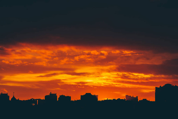 鮮やかな炎のような夜明けの街並み。驚くほど暖かい劇的な曇り空都市の建物の暗いシルエットの上。オレンジ色の日差し。どんよりした天気で日の出の大気中の背景。コピー スペース. - 写真・画像