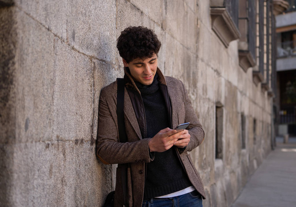 Muoti college mies parikymppisenä onnellinen tarkistaa blogin tai chattailuun internetissä ystävän kanssa älypuhelimella sovellus Euroopan kaupungin ulkona. Viestintätekniikka ja matkailu Euroopassa
. - Valokuva, kuva