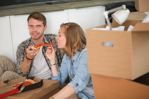 Casal jovem tem uma pausa para o almoço de pizza no chão depois de se mudar para uma nova casa com caixas em torno deles. Casal jovem - Foto, Imagem