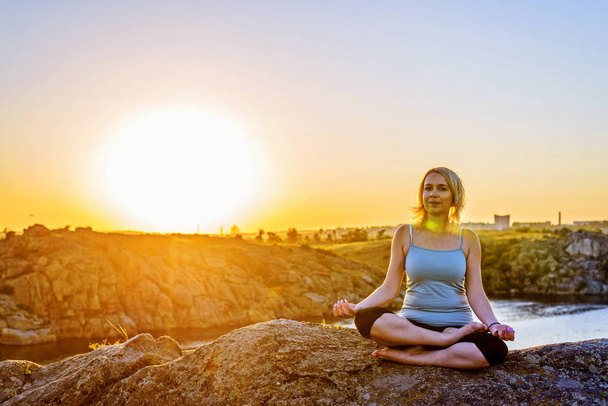 Young woman doing yoga on top of a mountain at sunset, free space. - 写真・画像