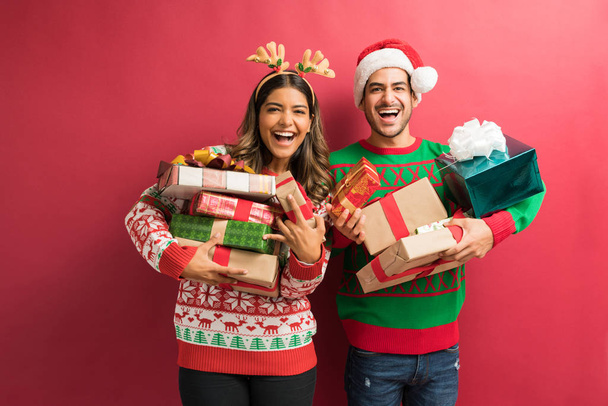 Portrait of cheerful attractive couple holding Christmas presents against plain background - Foto, imagen