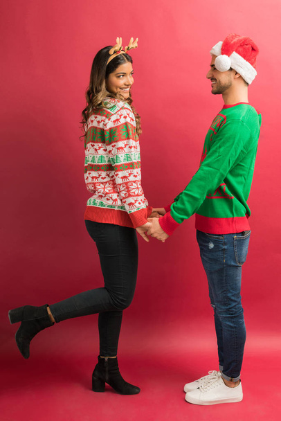 attraktive Frau, die auf einem Bein steht, während sie ihren Freund ansieht, der die Hände isoliert vor rotem Hintergrund hält - Foto, Bild