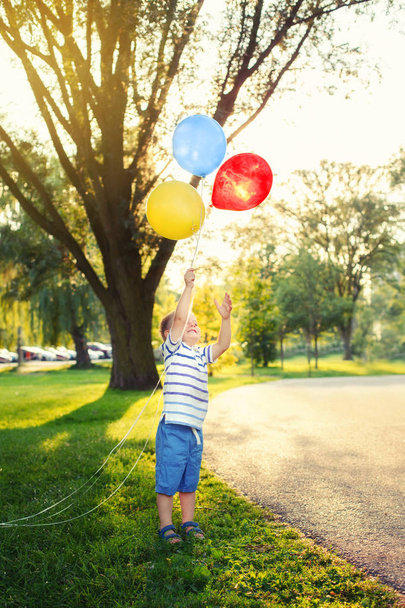 Cute adorable little Caucasian boy toddler child with colorful balloons in park outdoor. Kid enjoying playing. Happy birthday holiday celebration. Candid authentic lifestyle childhood moment. - Photo, Image