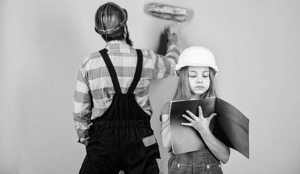 Kid girl planning renovation. Child renovation room. Family remodeling house. Little fathers helper. Father bearded man and daughter hard hat helmet uniform renovating home. Home improvement activity - Foto, afbeelding