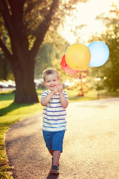 Lindo adorable niño pequeño caucásico niño pequeño con globos de colores en el parque al aire libre. Al chico le gusta jugar. Feliz fiesta de cumpleaños. Candid auténtico estilo de vida momento de infancia
. - Foto, Imagen