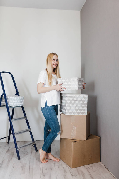 Young woman moving in her new house and doing a home makeover, she is standing near many cardboard boxes around - Фото, зображення