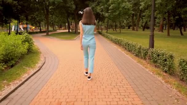 vista trasera alegre mujer caucásica caminando hablando por teléfono en la calle en el parque de la ciudad
 - Imágenes, Vídeo