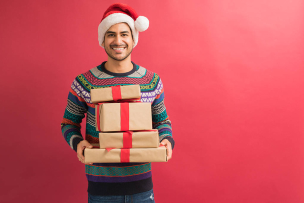 Portret van glimlachend jong aantrekkelijk Latin man Holding presenteert tijdens kerstviering geïsoleerd in Studio - Foto, afbeelding