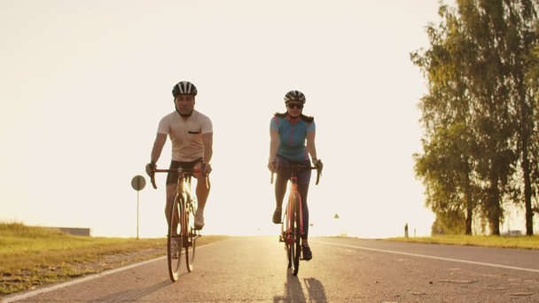 ein Mann und eine Frau fahren bei Sonnenuntergang mit Sportfahrrädern auf der Autobahn in Ausrüstung und Schutzhelmen in Zeitlupe 120 fps - Filmmaterial, Video