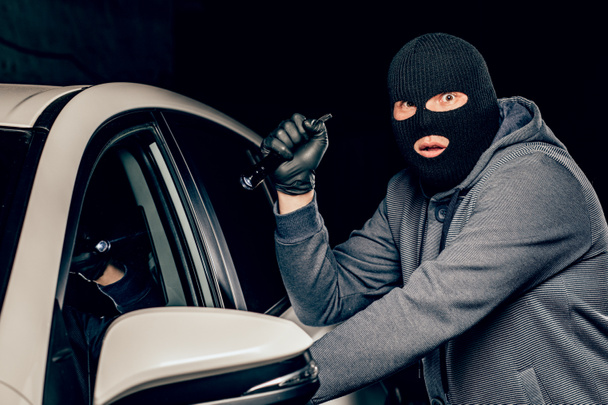 Un rapinatore vestito con una maschera nera, che punta una torcia alla dri
 - Foto, immagini