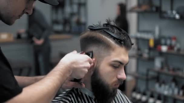 Close-up view on males hairstyling in a barber shop with professional trimmer. Mans haircutting at hair salon with electric clipper. Grooming the hair. - Felvétel, videó