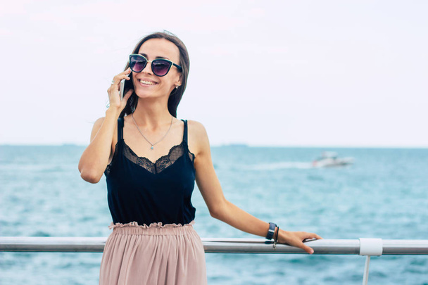 Cheerful brunette woman in sunglasses talking via smartphone - Фото, изображение