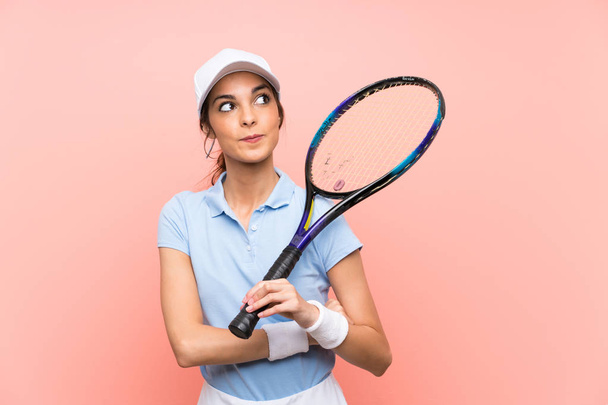 Jeune joueuse de tennis femme sur mur rose isolé levant les yeux tout en souriant
 - Photo, image