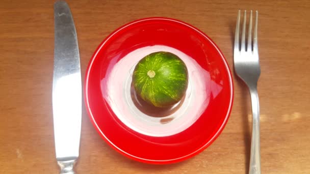 a tiny cucumber on a Red platter, but the cucumber is very similar to a small watermelon or planet Earth, next to a knife and fork, as if greedy people want to devour planet earth - Footage, Video