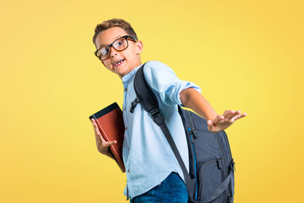 Student boy with backpack and glasses is a little bit nervous and scared on yellow background - Foto, Bild