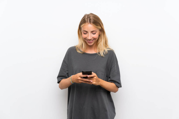 blonde junge Frau vor isoliertem weißen Hintergrund sendet eine Nachricht mit dem Handy - Foto, Bild