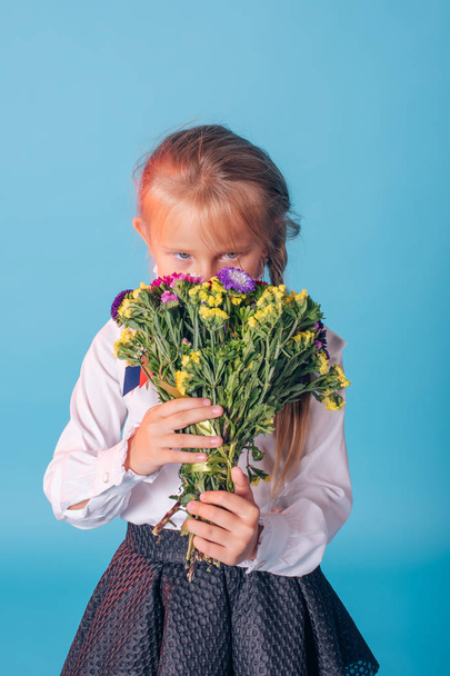 Portrait of beautiful young first-grader. First-grader girl in the studio with flowers - Photo, Image