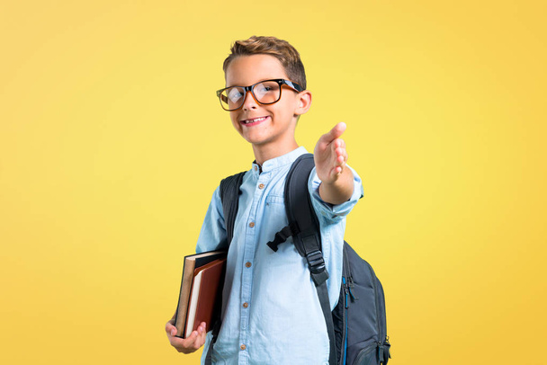 Étudiant garçon avec sac à dos et lunettes poignée de main après une bonne affaire sur fond jaune
 - Photo, image