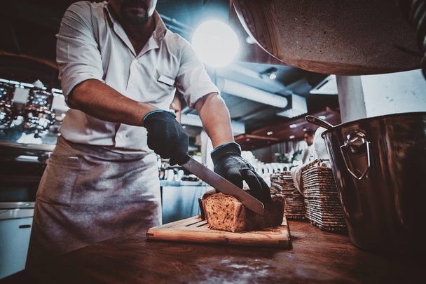 Küchenhelfer schneidet Brot für das Mittagessen - Foto, Bild