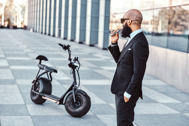 Элегантный мужчина курит рядом со своим электро-велосипедом
 - Фото, изображение