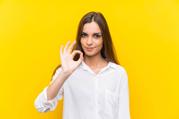 Mujer joven sobre fondo amarillo aislado mostrando un signo de ok con los dedos
 - Foto, Imagen