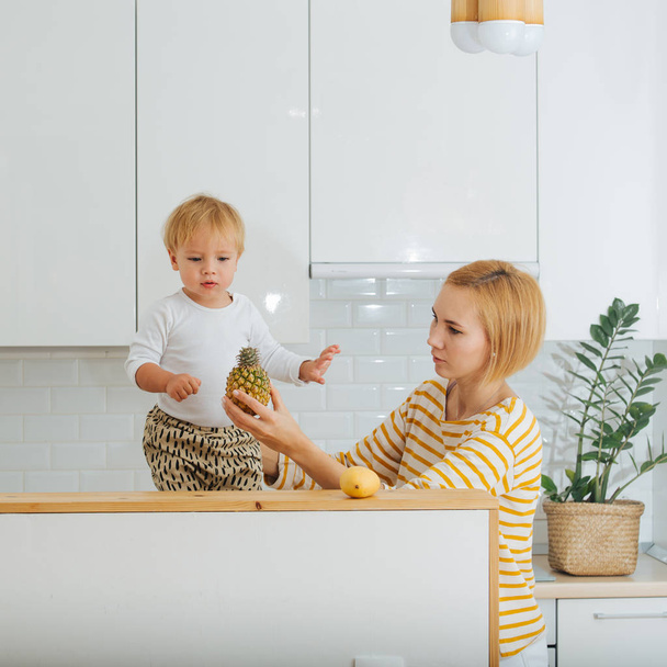 Jolly blond toddler boy is offered pineapple - Foto, afbeelding