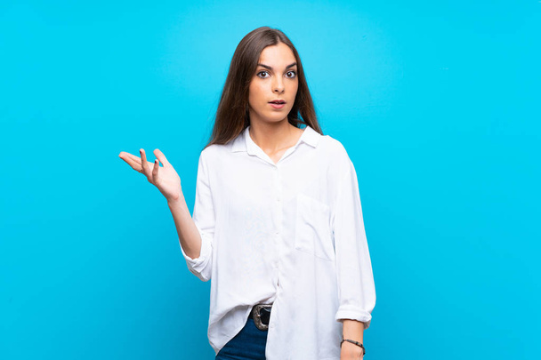 Young woman over isolated blue background making doubts gesture - Фото, зображення