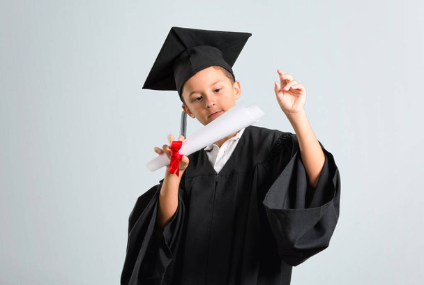 Little boy graduating smiling and showing victory sign on grey background - Fotoğraf, Görsel
