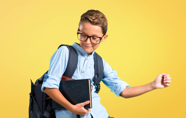 Student jongen met rugzak en bril luisteren naar de muziek en dansen op gele achtergrond - Foto, afbeelding