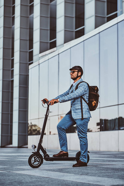 El hombre está conduciendo su nuevo scooter eléctrico cerca de un gran edificio de vidrio
 - Foto, Imagen