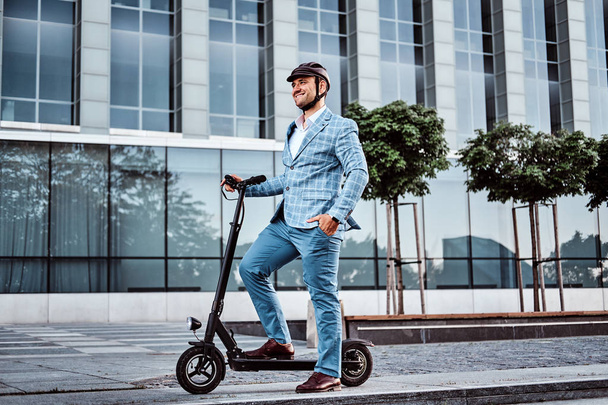 Handsome man is riding his scooter near offices building - Foto, Bild