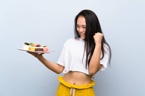 Teenager asian girl holding lots of different mini cakes celebrating a victory - Foto, imagen