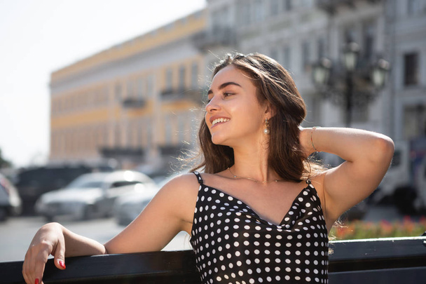 Mooie jonge vrouw in een zwarte jurk zit op een bankje rusten na sightseeing tour in de oude Europese stad. - Foto, afbeelding