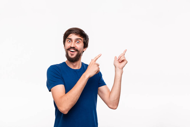 Handsome brunet man in a blue shirt with beard and mustaches pointing with his fingers to the left corner standing isolated over white background. Place of product and advertisment. - Photo, Image