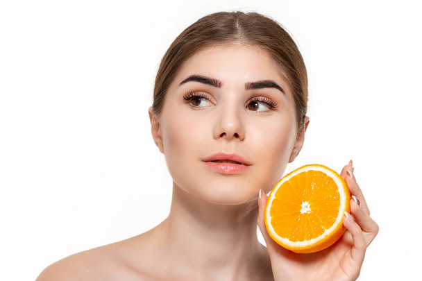 Retrato de cerca de una joven hermosa y feliz sosteniendo la mitad de las naranjas cerca de la cara aislada sobre fondo blanco
. - Foto, imagen