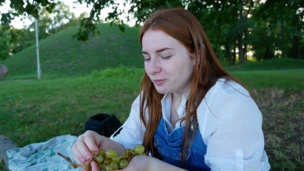 Vöröshajú lány eszik gyümölcsöket a nyár a parkban - Felvétel, videó