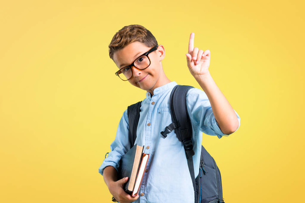 Student boy with backpack and glasses counting number one sign on yellow background - Foto, imagen