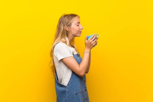 Blonde jeune femme sur fond jaune isolé tenant tasse de café chaud
 - Photo, image