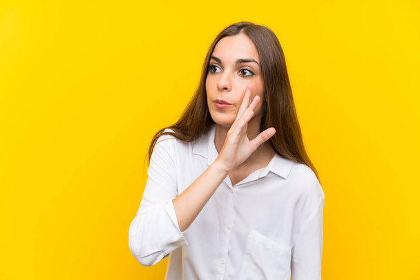 Young woman over isolated yellow background whispering something - Foto, afbeelding