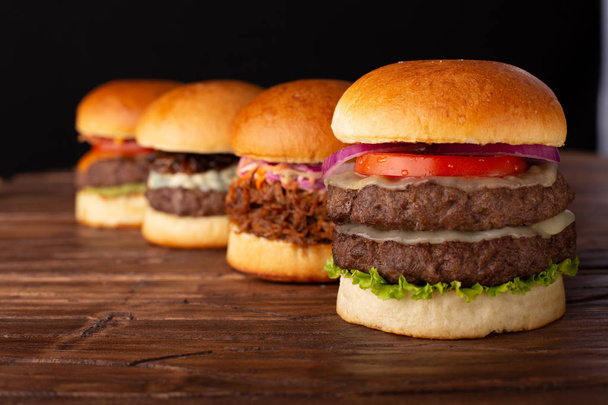 Cztery różne hamburgery w rzędzie umieszczonym na drewnianym stole - Zdjęcie, obraz