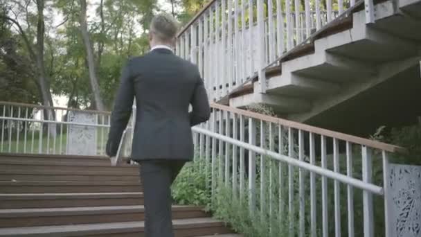 Successful stylish young businessman in expensive suit and shoes walking upstairs. Office lifestyle, business concept. The man in the suit holding a laptop walking outdoors. Climbing stairs. - Záběry, video